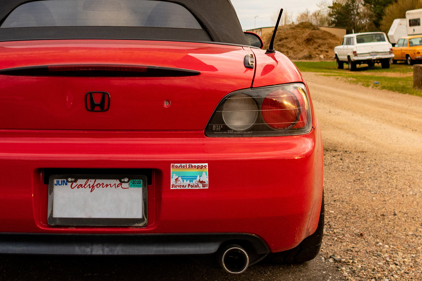 Image of Hostel Shoppe bumper sticker on rear bumper of a red Honda car with California license plate.