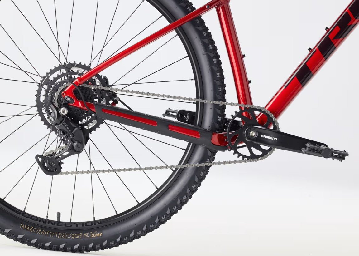 Close-up of a red Trek Marlin 5 mountain bike with chain and gear system on a white background.