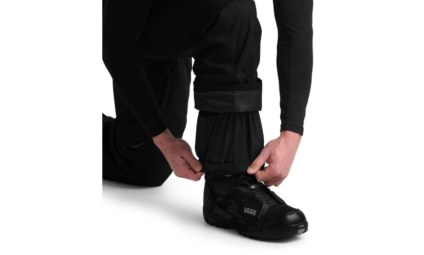 Studio image of person adjusting elastic cuff of black snowpants over snowboard boots