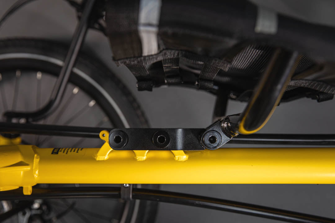 Close up view of black seat extender under a seat, attached to a yellow frame.