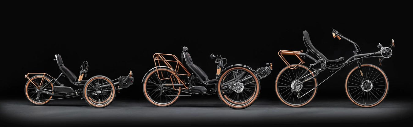 Studio image of a small recumbent trike a medium recumbent trike and a two wheel recumbent bike, all with black frames and tan highlights