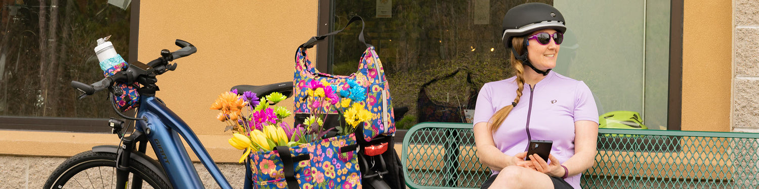 A woman sits by her bike featuring Po Campo bike bags filled with flowers.