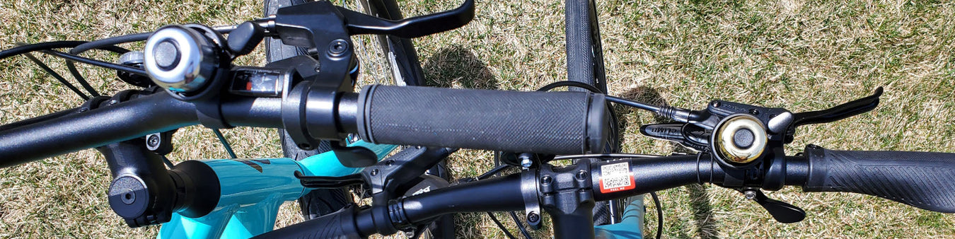 Two bicycle handlebars featuring a gold bell and a silver bell.