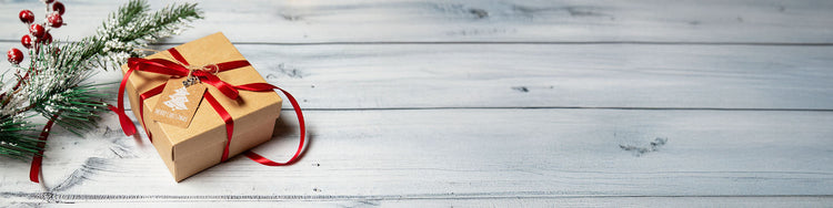 A Christmas present and a pine bough against a grey wooden background.