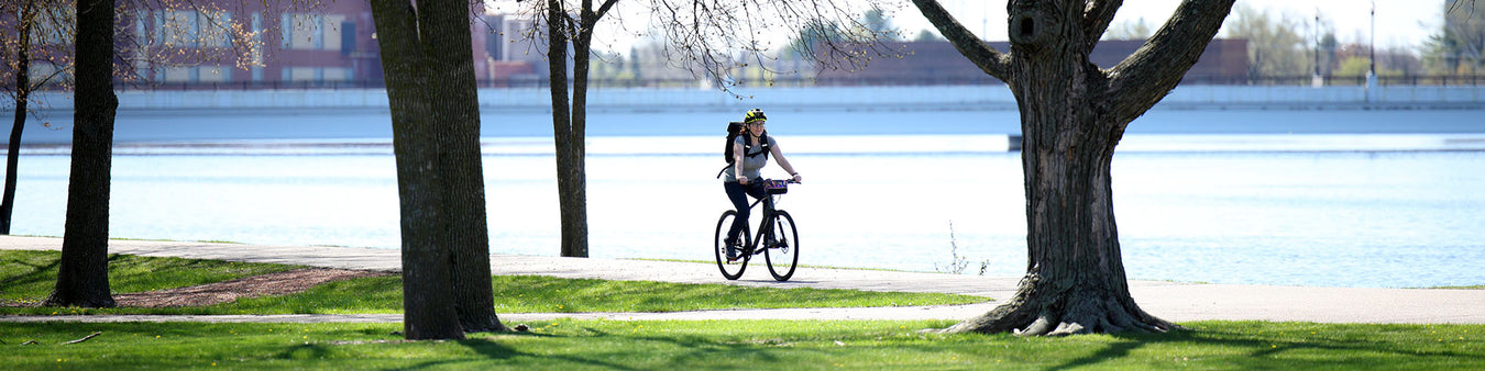 A women rides down the bike path along a river wearing a backpack.