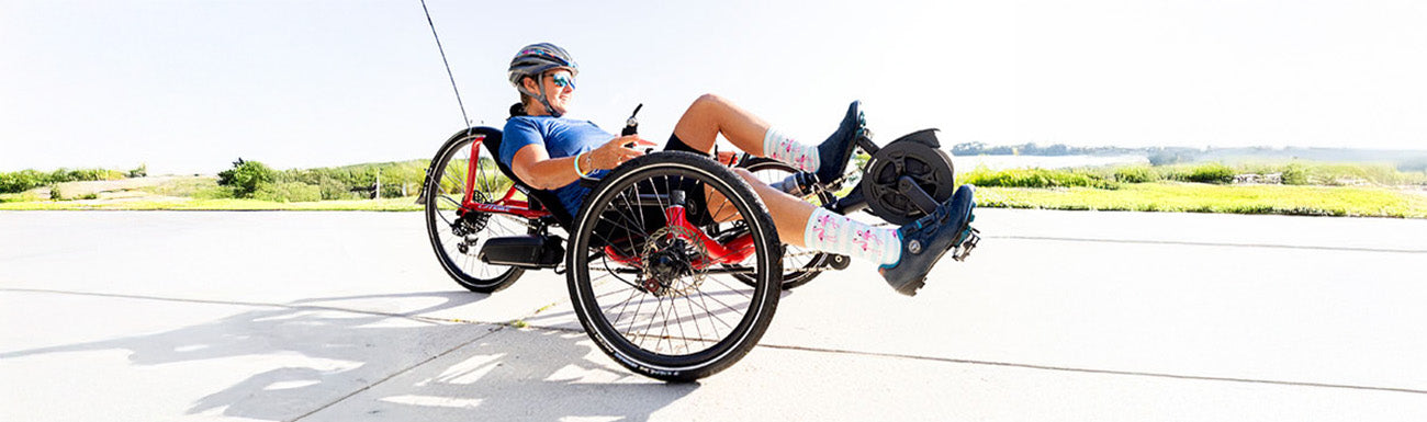 A man rides an e-assist recumbent Catrike down a bike path. 