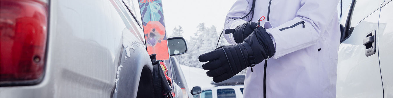 A women puts on a pair of gloves outside her car in winter.