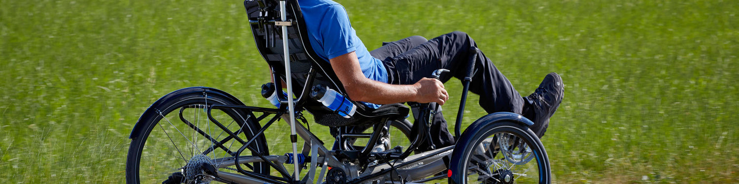 A man rides an HP Velotechnik trike with a bunch of accessories on it, including water bottle cages and water bottles.