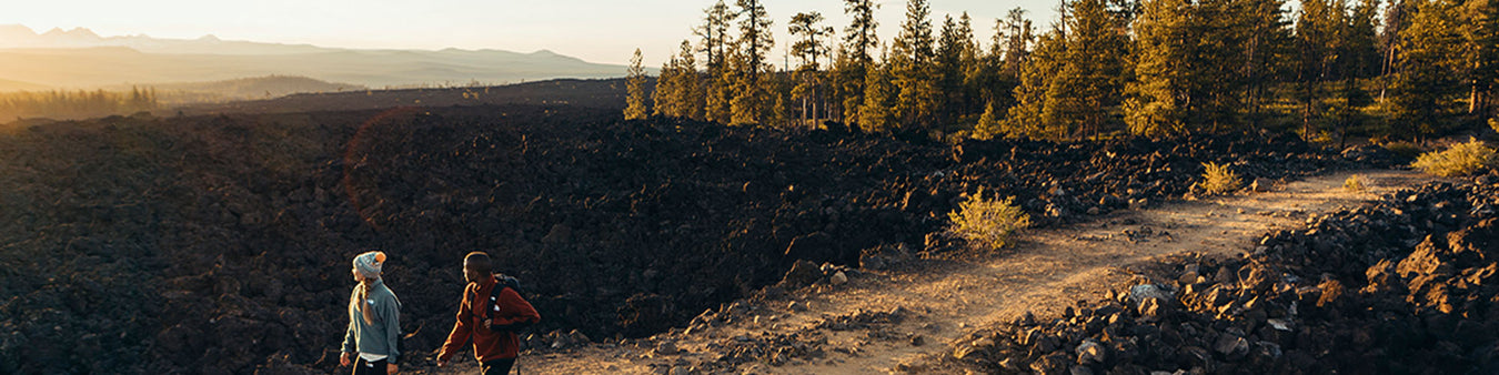 Two hikers walk along a rocky path watching the sunset.