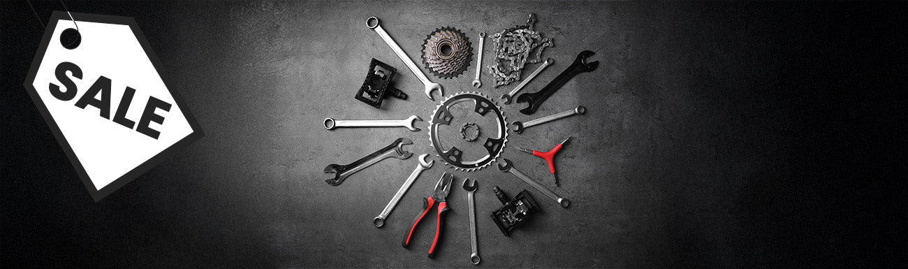 An assortment of bike repair tools and parts against a gradient black background. A black and white "sale" graphic overlays the image.