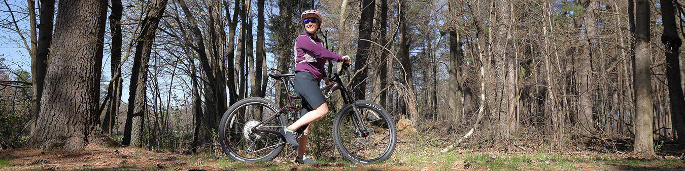 A woman rides a mountain bike in a wooded setting.