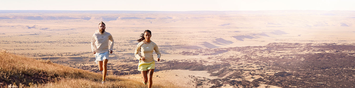 Two joggers run through a desert landscape.