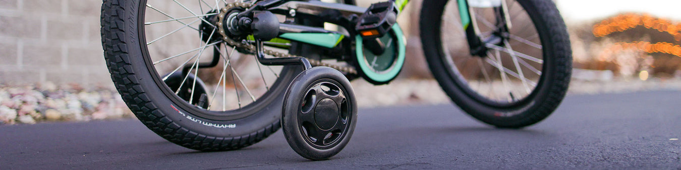 A kid's bike has a set of black training wheels on it.