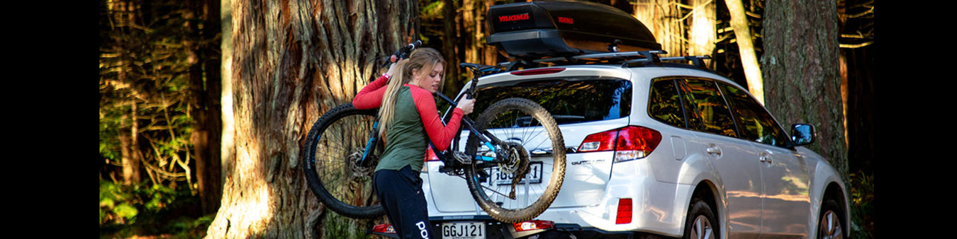 A girl removes a bike from her car's Yakima Hitch rack.  She also has a Yakima cargo box on her car's roof.