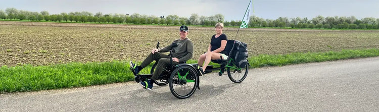 A couple rides a Bambuk tandem in the countryside along the road by an open field.