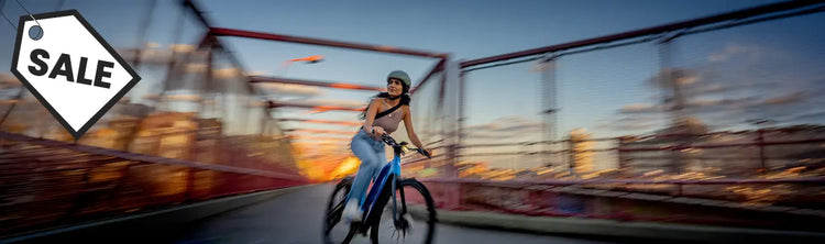 A woman rides a bike across a bridge and there is the black and white sale tag in the corner.