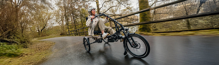A woman rides a Hase Kettwiesel One Up down a road in the fall.