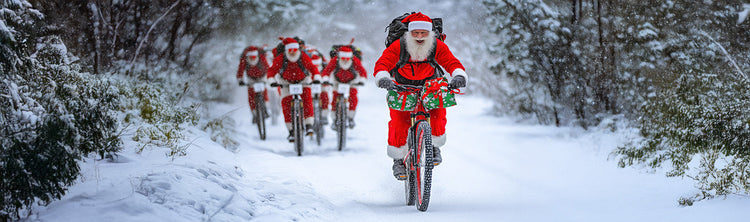 A group of Santa's ride through a snowy landscape on mountain bikes.