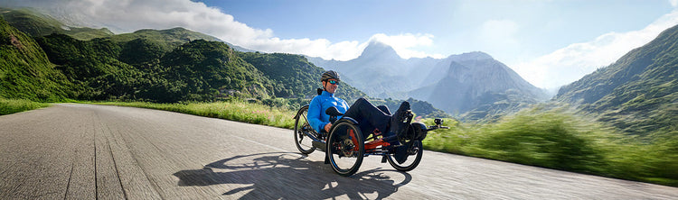 A man rides an HP Velotechnik Scorpion fs 26 recumbent trikes on a road through the mountains.