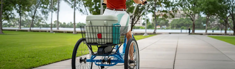 A woman rides a Sun Bicycles electric assist trike to the park along a treelined riverway.