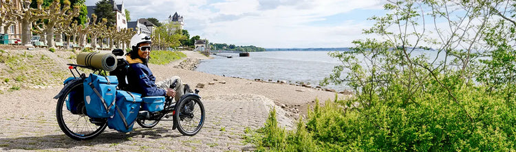 A man on an HP Velotechnik Scorpion trike has racks and panniers for touring, while he takes a break in a town alongside a lake.