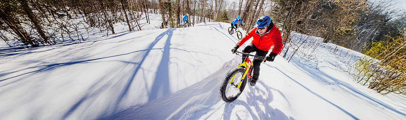 Fat bikers ride through the snow on a sunny day.