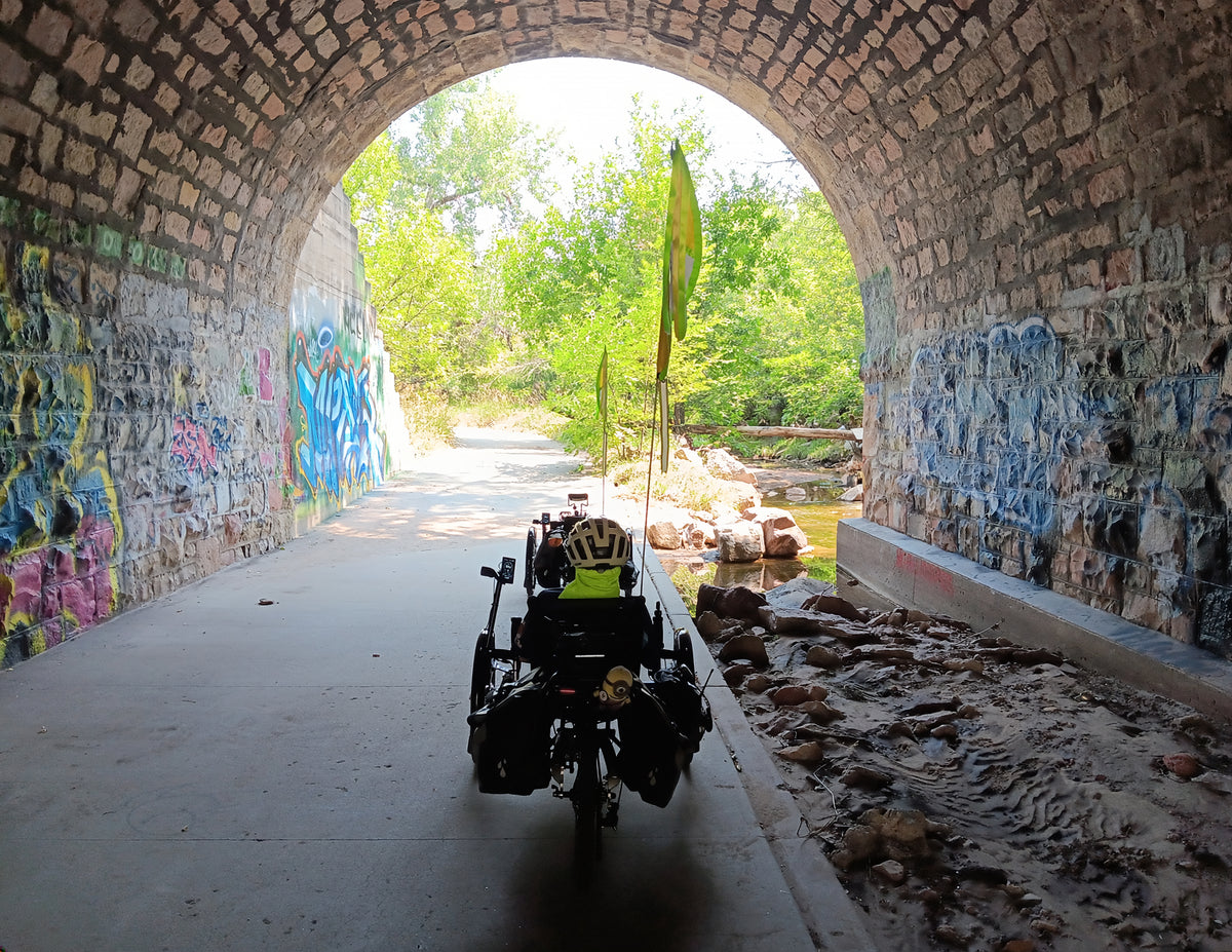 Two recumbent trikes are pictured in a stone tunnel with grafitti on the walls.