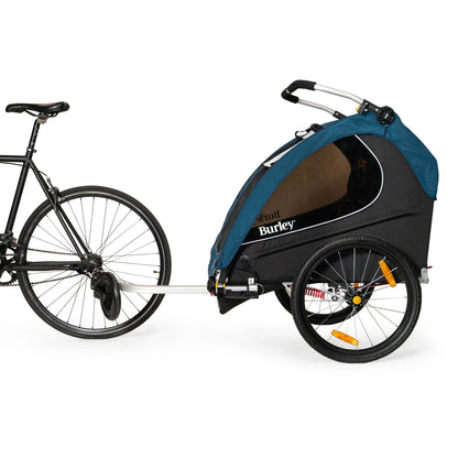 Side view of the Burley Encore X Child Trailer in Blue, shown connected to a bicycle, on a white background.
