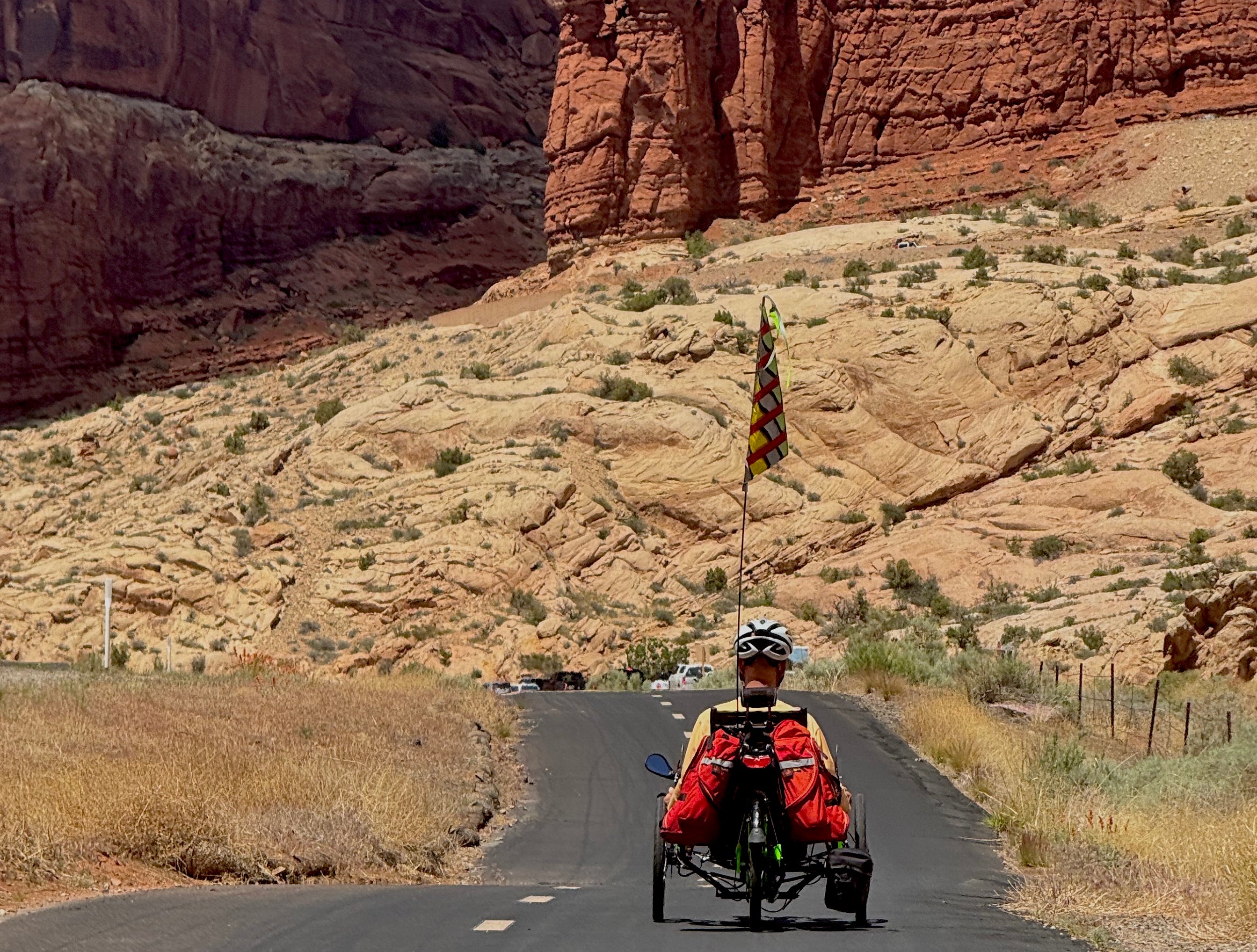 Person riding a recumbent trike on a desert road with red rock formations.