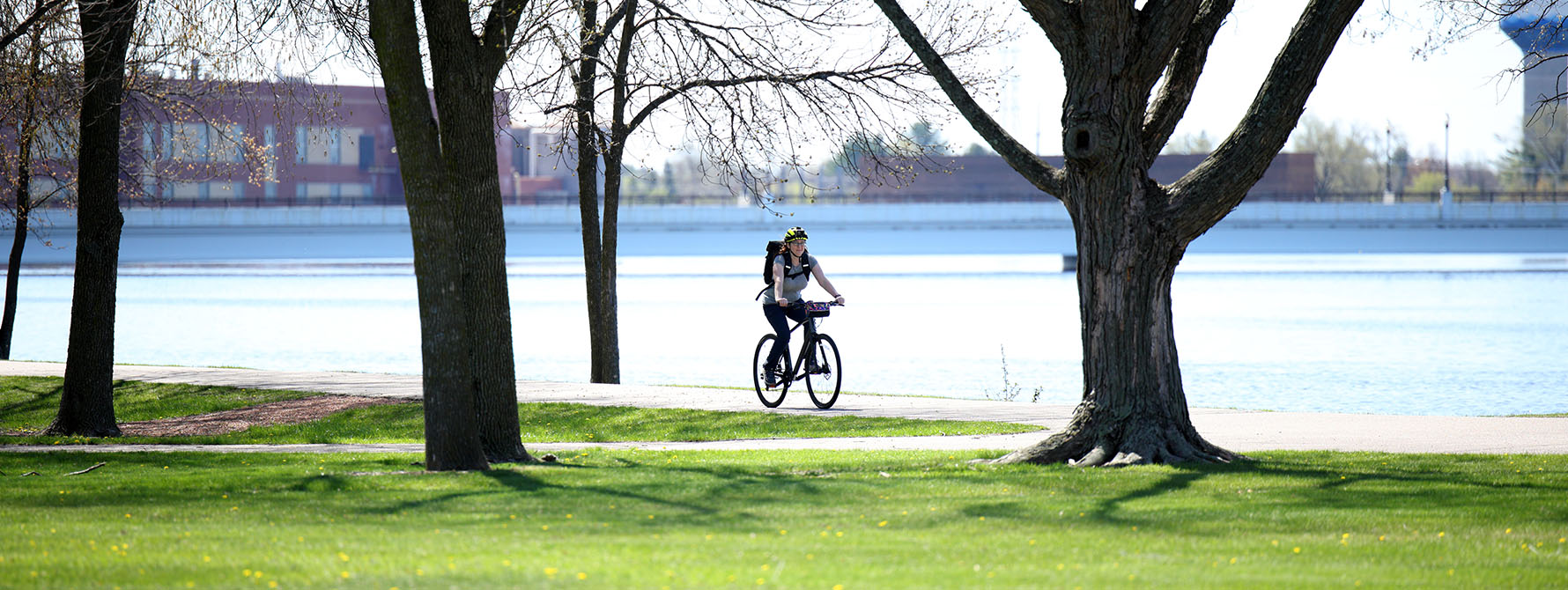 A woman commutes down a bike path along a river with a backpack on her back.