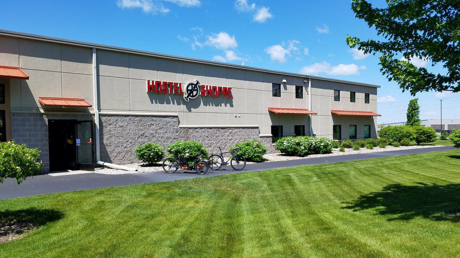Photo of recumbent trike and traditional bike in front of the Hostel Shoppe building on a bright Spring day.