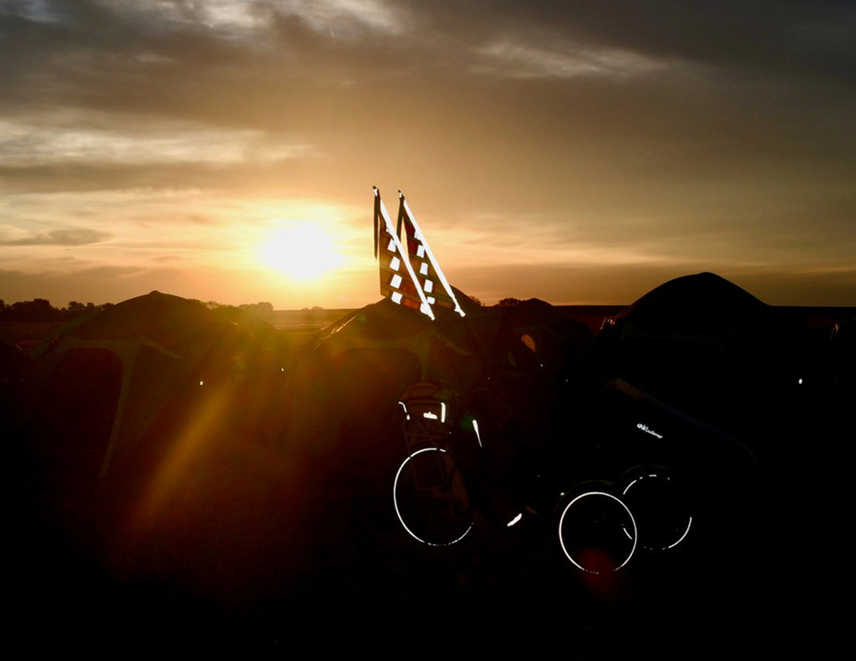 A trike is silhouetted by it's reflective elements with a sunrise in the background.