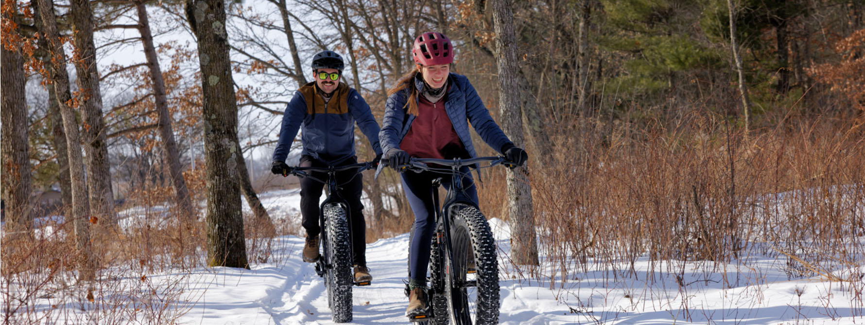 Two cyclists ride fat bikes through the snowy woods on a sunny day!