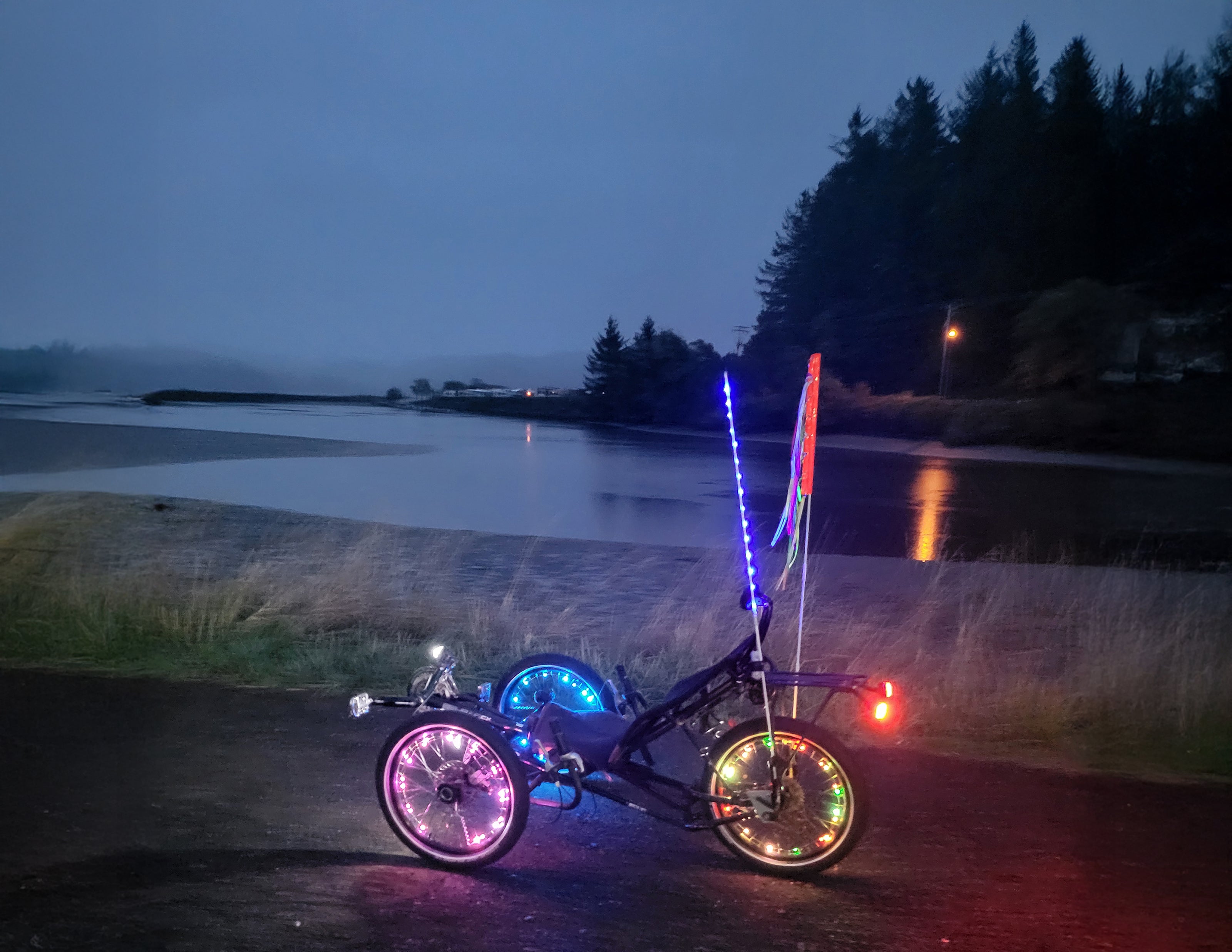 A recumbent trike all lit up in front of a scenic bay at dusk.