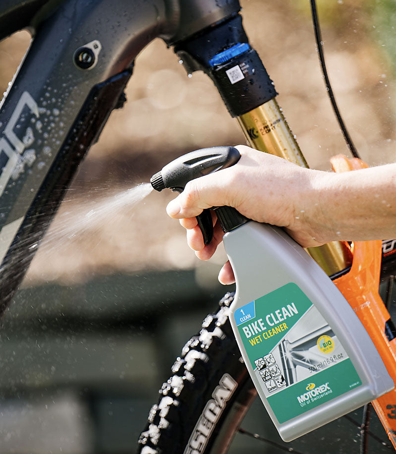 Person using a bottle of Motorex Bike Clean spray on a mountain bike.