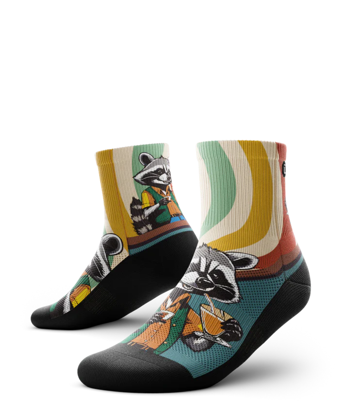 Multicolored pair of socks with racoon wearing brown button down shirt and green vest drinking cups of coffee. Swirled cuff of green, cream, yellow and red. Black soles