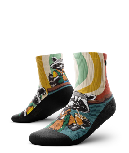 Multicolored pair of socks with racoon wearing brown button down shirt and green vest drinking cups of coffee. Swirled cuff of green, cream, yellow and red. Black soles