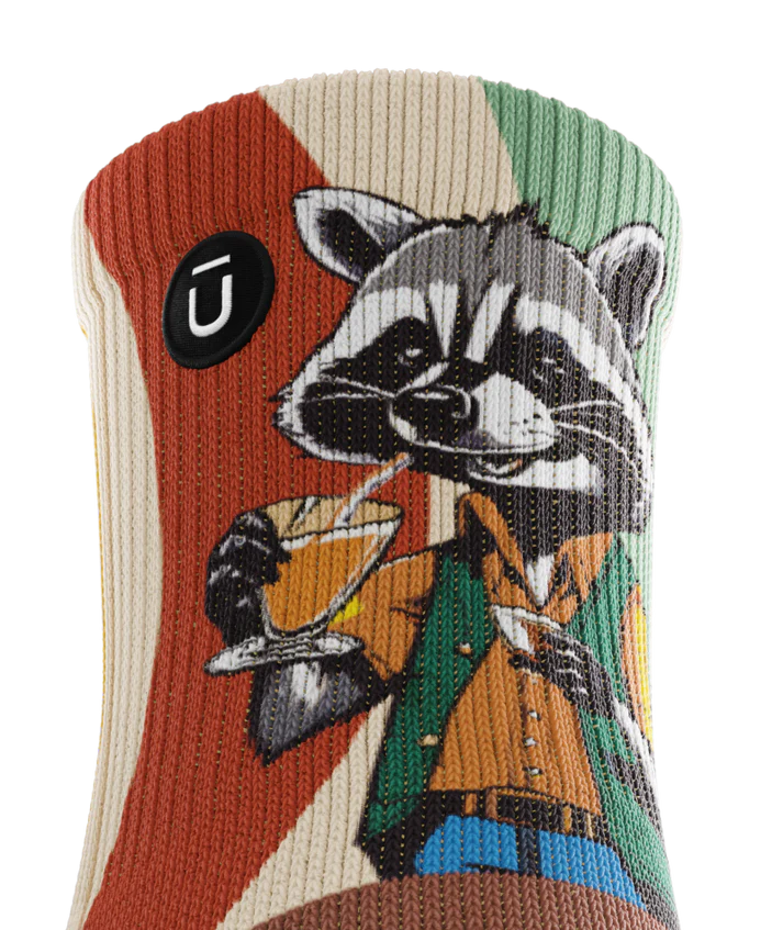 Top cuff view of  a multicolored  sock with racoon wearing brown button down shirt and green vest drinking cups of coffee. Small black circular logo with Outway logo near top of cuff. 