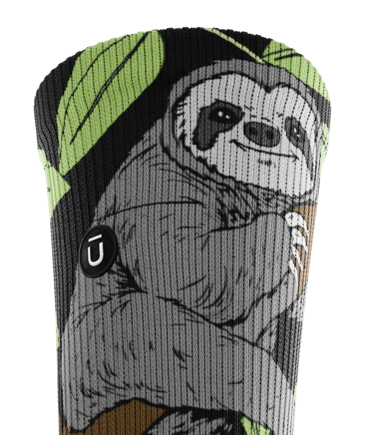 Top of cuff view of sock with sloths in trees on main part of sock. Small black circular patch with Outway logo on top third of cuff. 