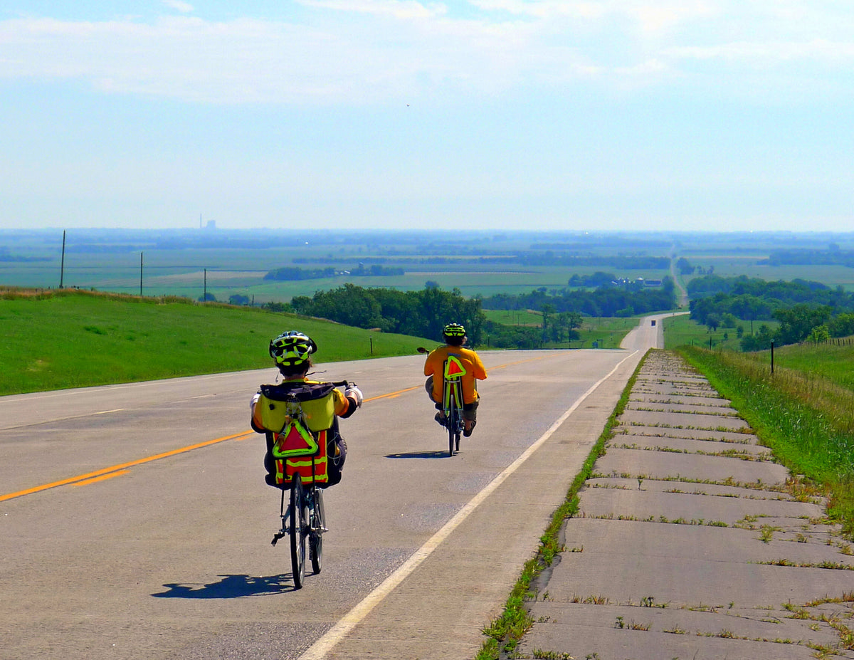 Two recumbent riders ride down a hill with a scenic green landscape in the background.