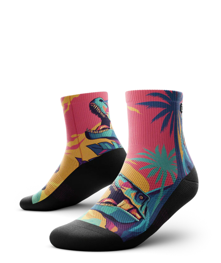 Multicolored  pair of socks with T-rex dinosaurs and palm trees on main part of sock, black soles. 
