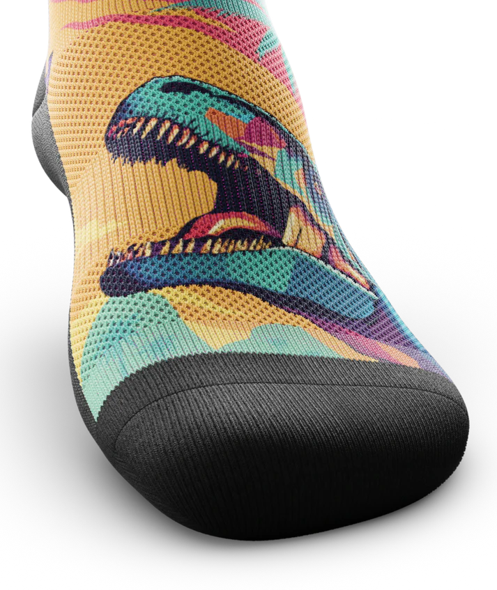 Top toe area of Multicolored sock with T-rex dinosaurs and palm trees on main part of sock, black soles. 