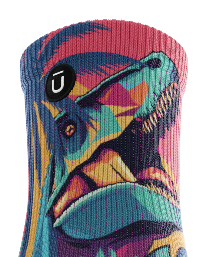 Top cuff of multicolored sock with T-rex and palm trees.  Small black circular patch with Outway logo on top third of sock.