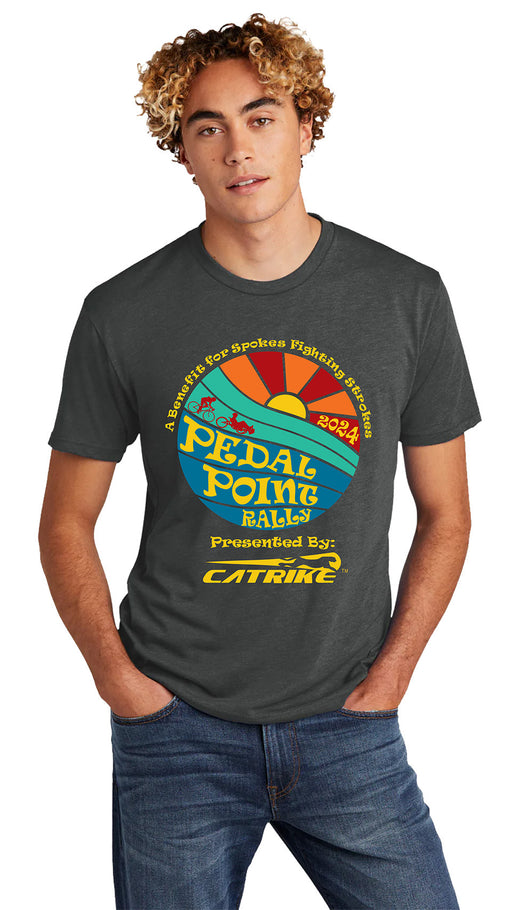Model wearing 2024 Pedal Point Rally Vintage Heavy Metal Event Tee front studio image with retro round image of sunset with red silhouette of biker and recumbent rider in red.  Image colors are orange, red and yellow sunset, turquoise and blue foreground with yellow lettering 