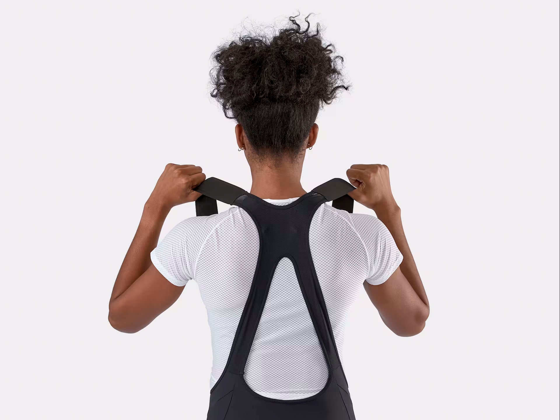 Studio rear strap detail view of a woman wearing black bib shorts over a white t-shirt. Woman is pulling up on the straps to highlight their flexibility. 