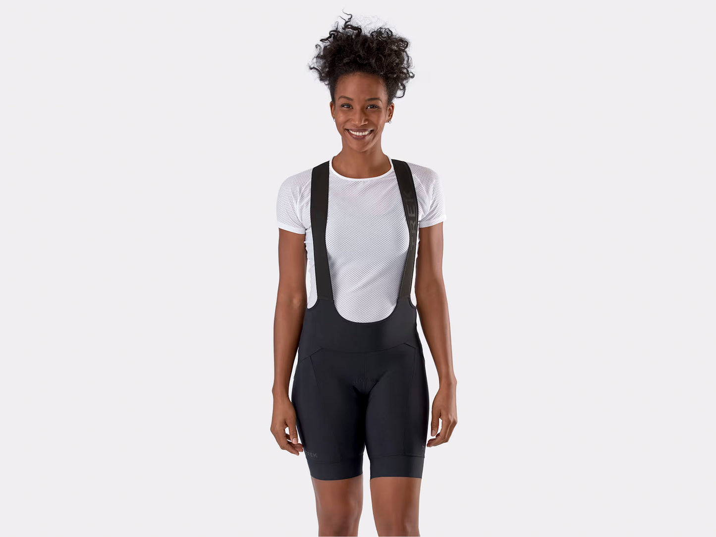 Studio front view of woman wearing black bib shorts over a white t-shirt. The straps of the bibs have Trek embossed along them.