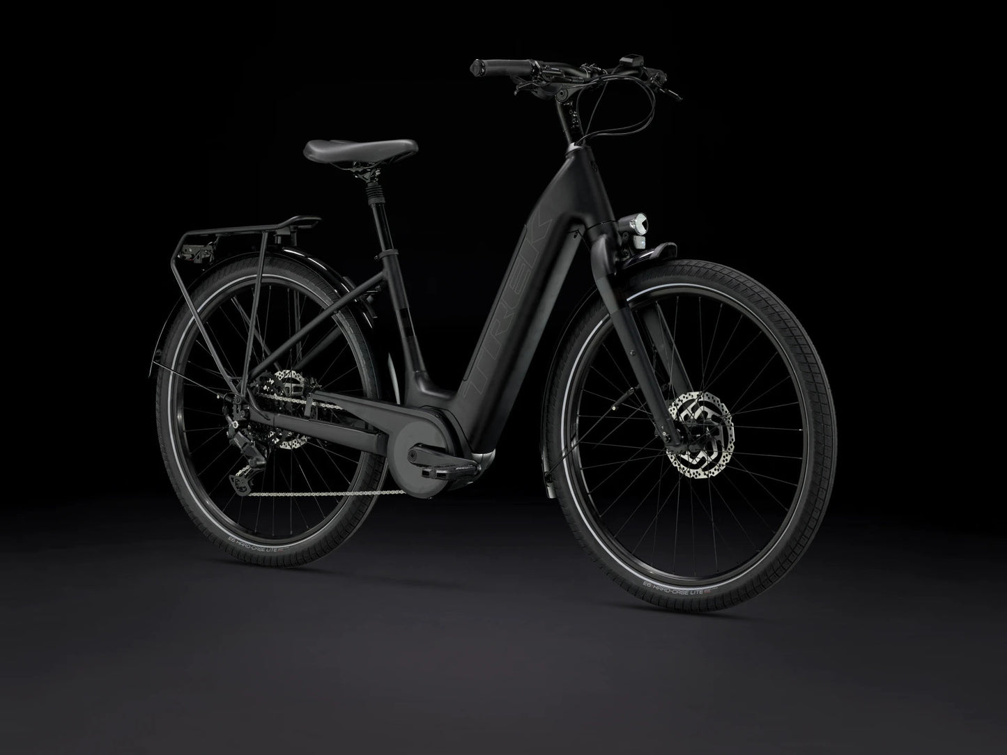Front quarter view of the Trek Verve+ 3 Lowstep Gen 3 e-Bike in Black, shown on a black background. It includes fenders, lights, rear rack, suspension seatpost, and kickstand.