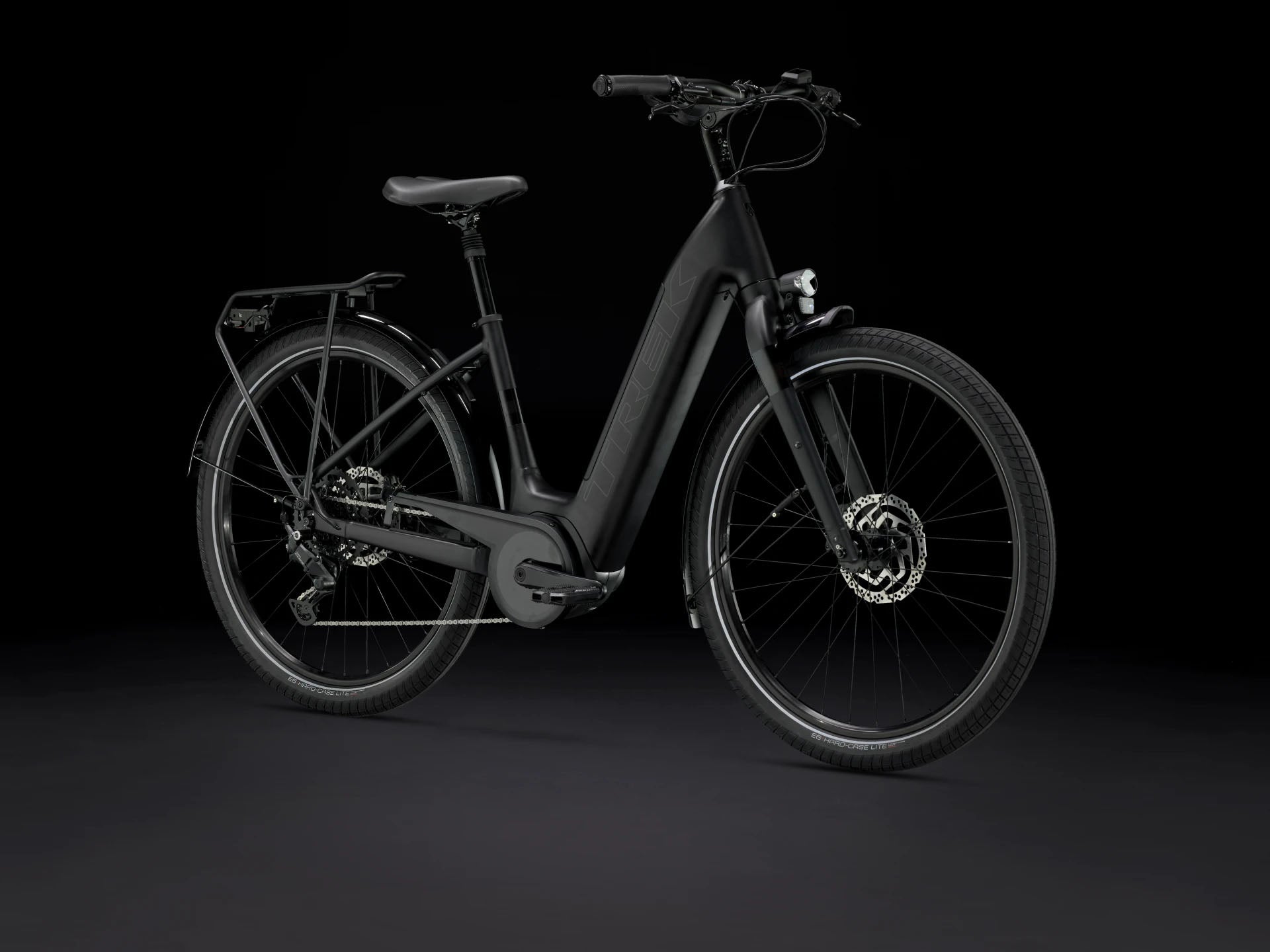 Front quarter view of the Trek Verve+ 3 Lowstep Gen 3 e-Bike in Black, shown on a black background. It includes fenders, lights, rear rack, suspension seatpost, and kickstand.