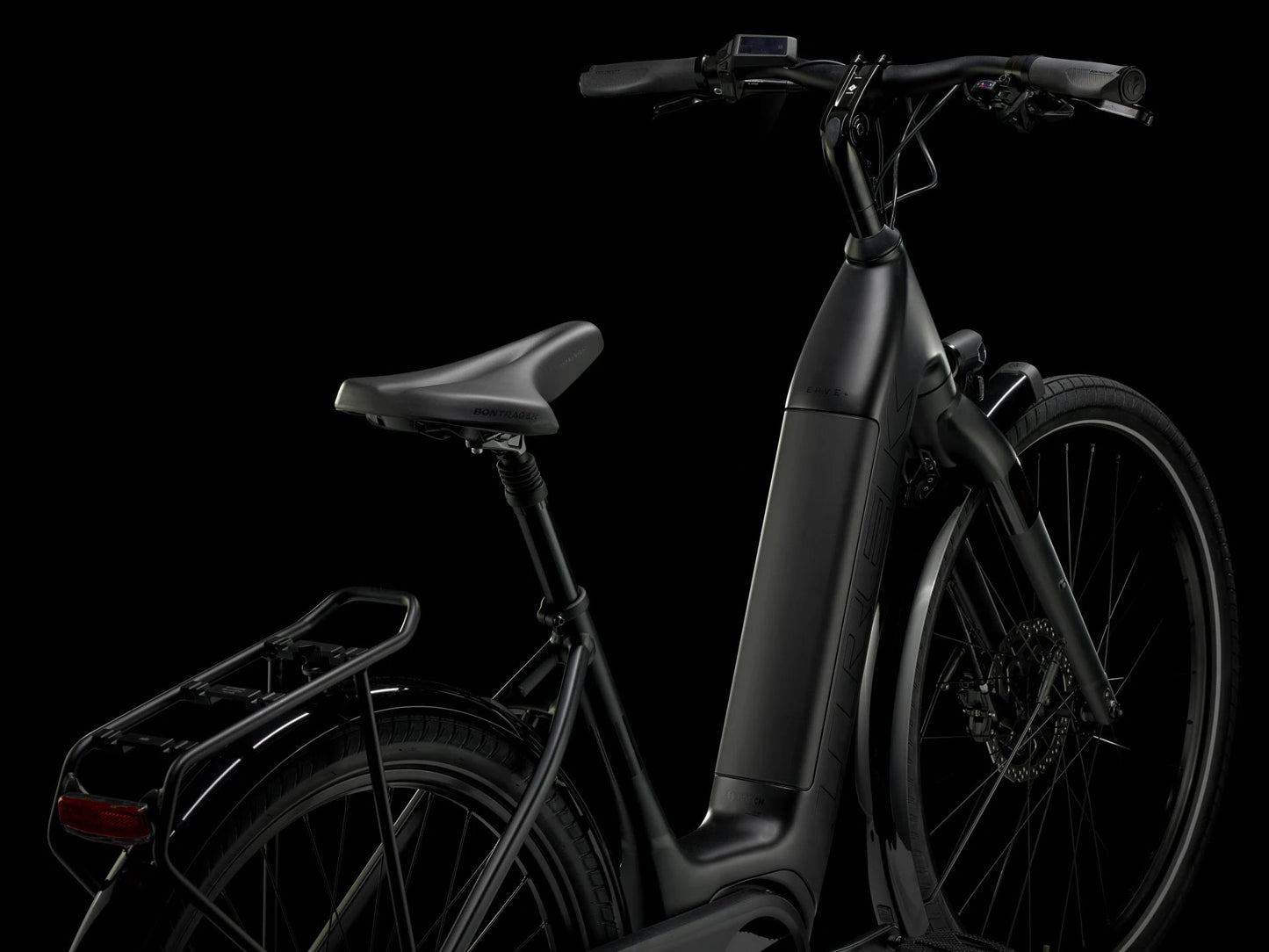 Rear quarter view of the Trek Verve+ 3 Lowstep Gen 3 e-Bike in Black, shown on a black background. It includes fenders, lights, rear rack, suspension seatpost, and kickstand.
