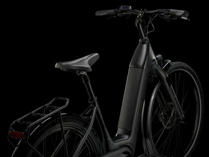 Rear quarter view of the Trek Verve+ 3 Lowstep Gen 3 e-Bike in Black, shown on a black background. It includes fenders, lights, rear rack, suspension seatpost, and kickstand.